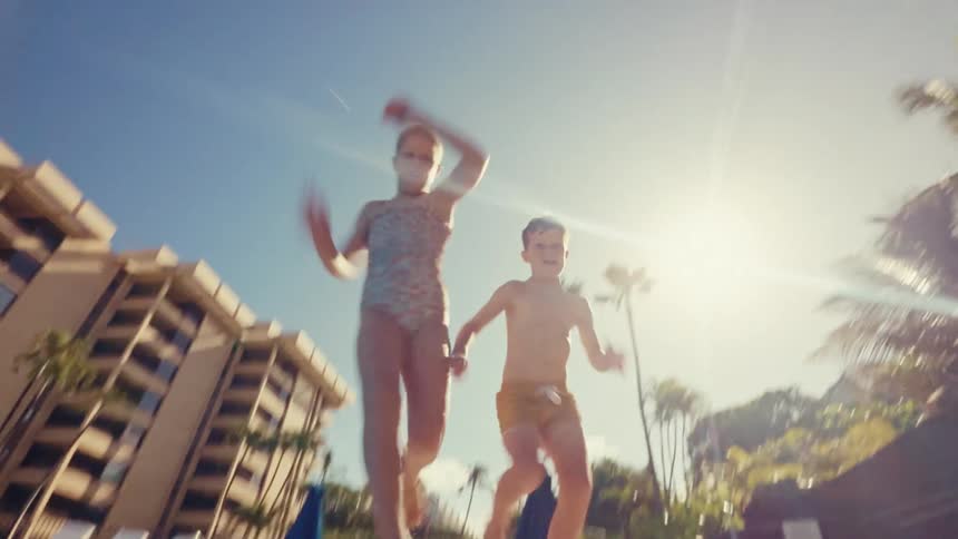 Siblings running and jumping into pool at resort on vacation