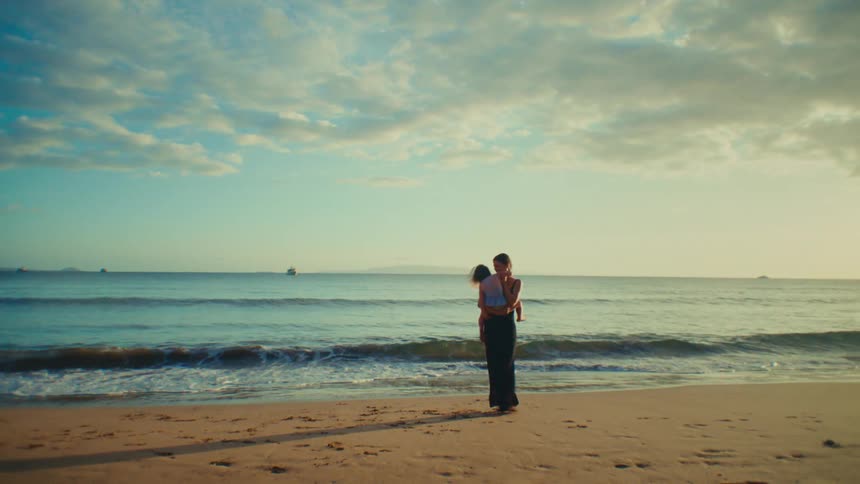 Mother standing on the beach spins while holding her daughter on a cloudy day