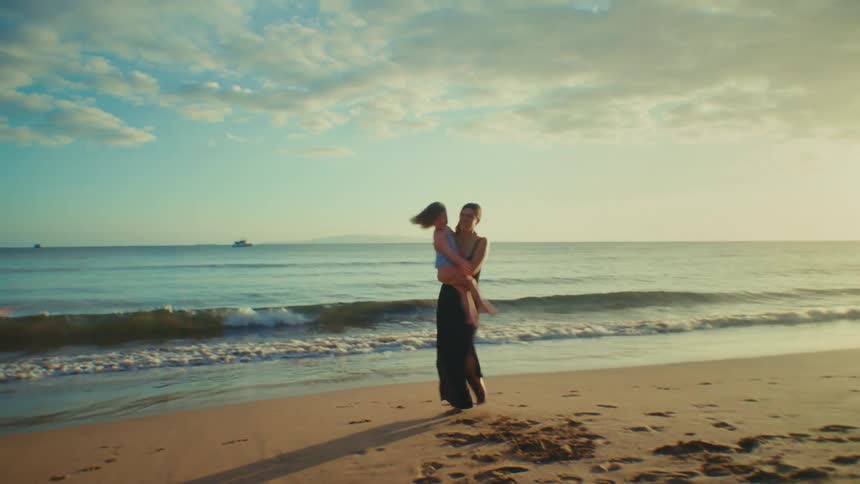 Mother holds her daughter and twirls around in front of the waves at the beach