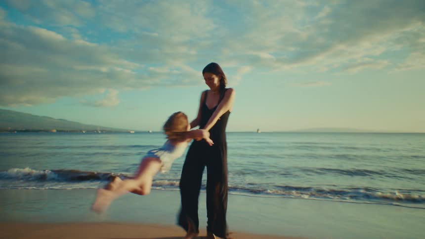 Mother spinning young daughter by the arms near the shoreline