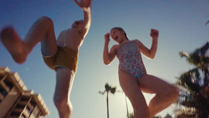 A boy and girl jump into a pool on a sunny day during a hotel vacation