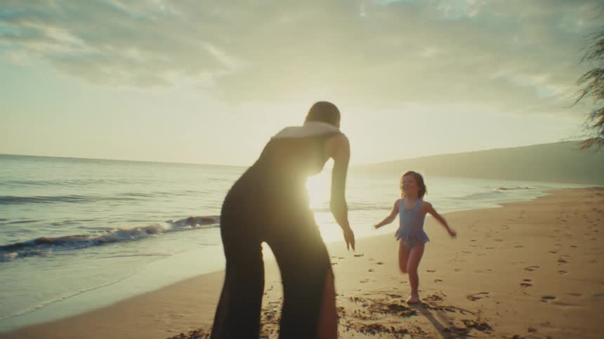 A little girl runs and jumps into her mothers arms on a beach