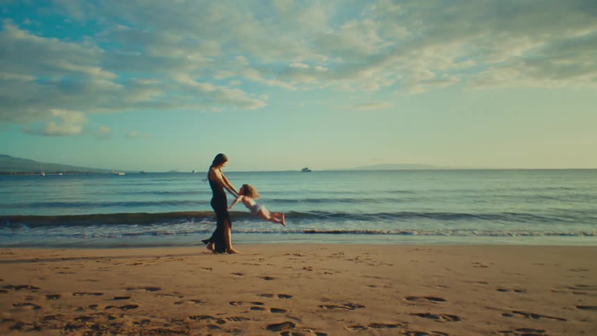 A mother holding her daughters arms and spinning her around on a sandy beach