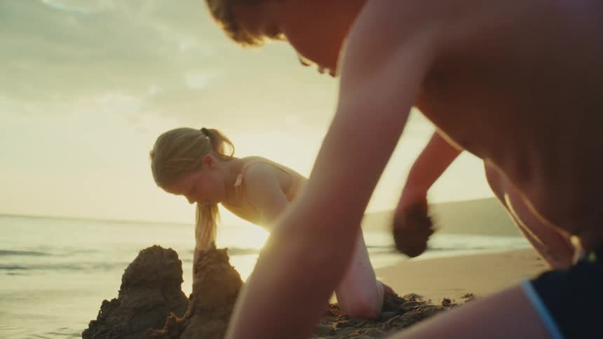 Two children are digging in the sand to make sandcastles at the beach