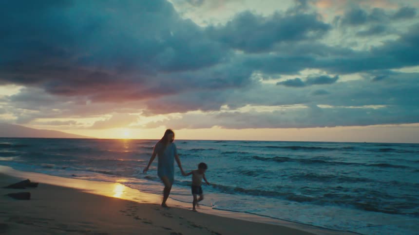 Mother and son run on the beach at sunset
