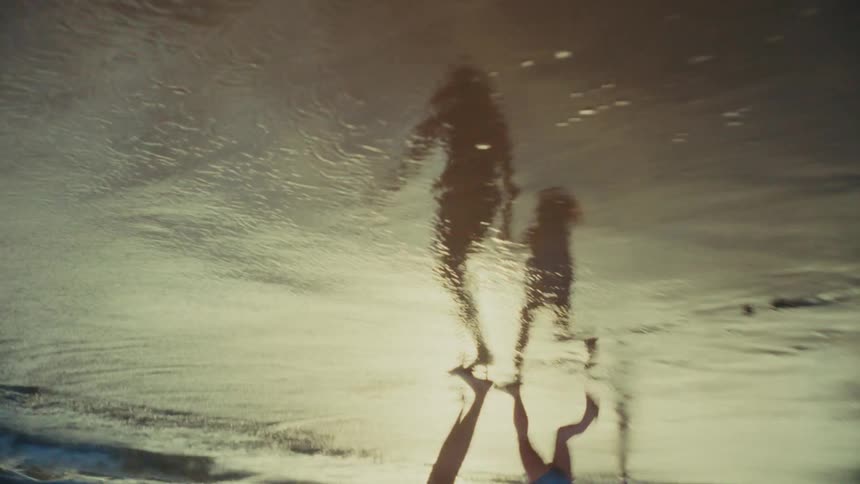 A mother and daughter walk into the water on the beach