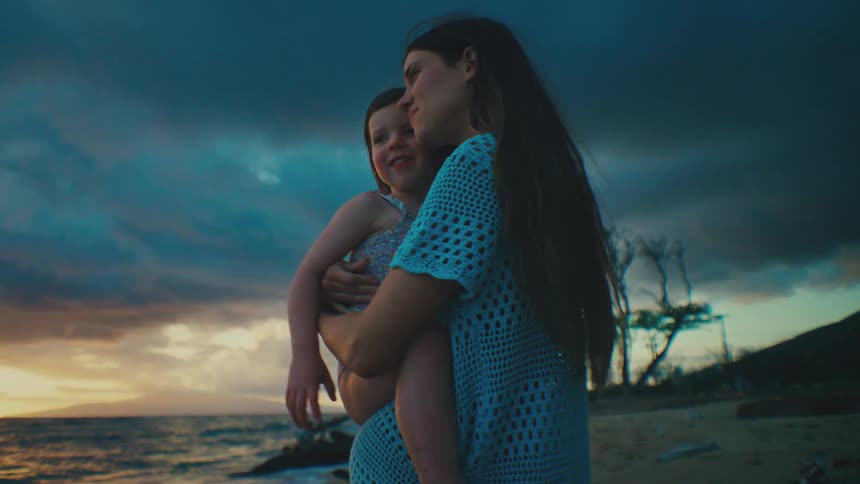 Mother holds daughter in her arms against a backdrop of a dramatic cloudy sky