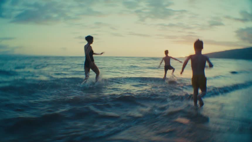 Mother and two young sons running together on tropical beach at sunset