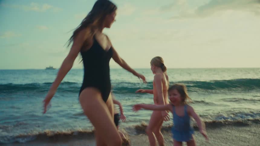 A mom and her daughters run and dance in the water at a beach