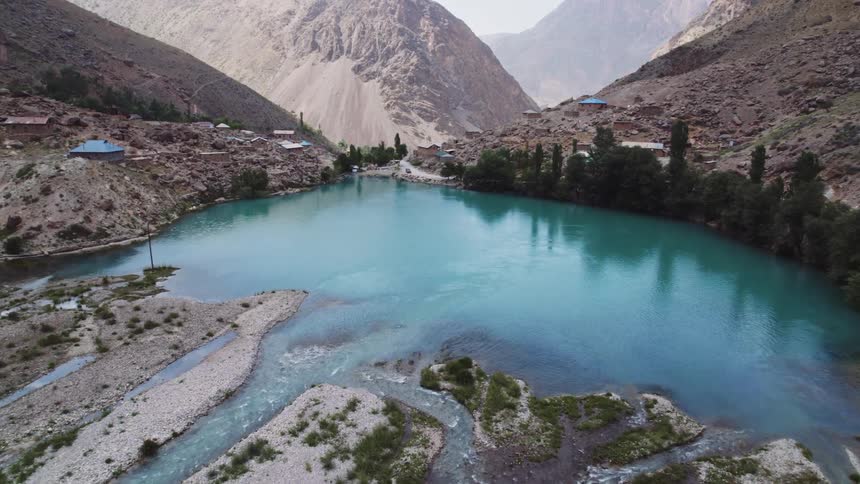Multiple streams end in a small lake of blue water near rural mountain homes