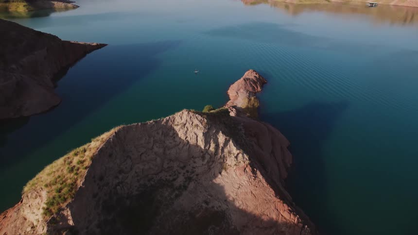An aerial perspective showcases a body of water with a prominent rock formation and in the waters surface a person is shown standup paddleboarding
