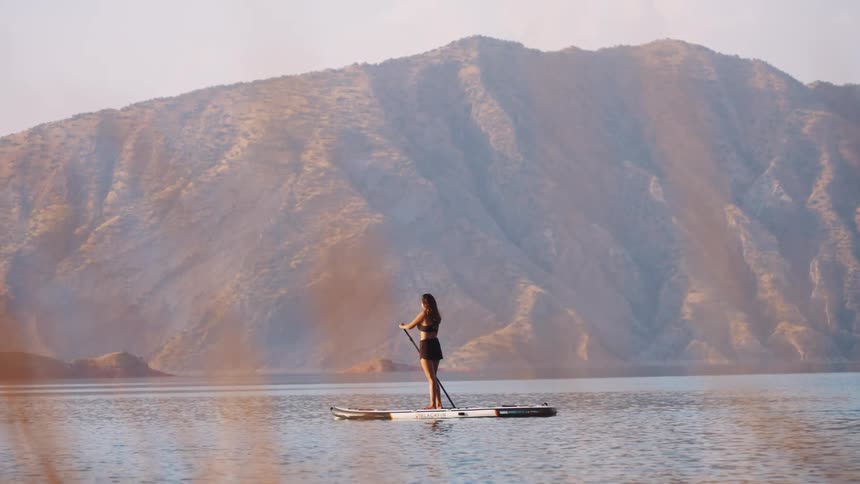 Female paddleboarding on lake with mountains in the background