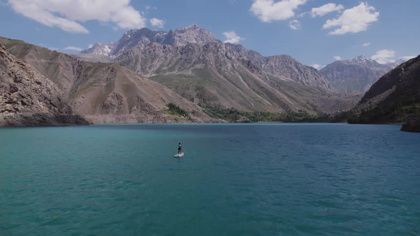 A woman is riding a paddle board across a lake in the mountains