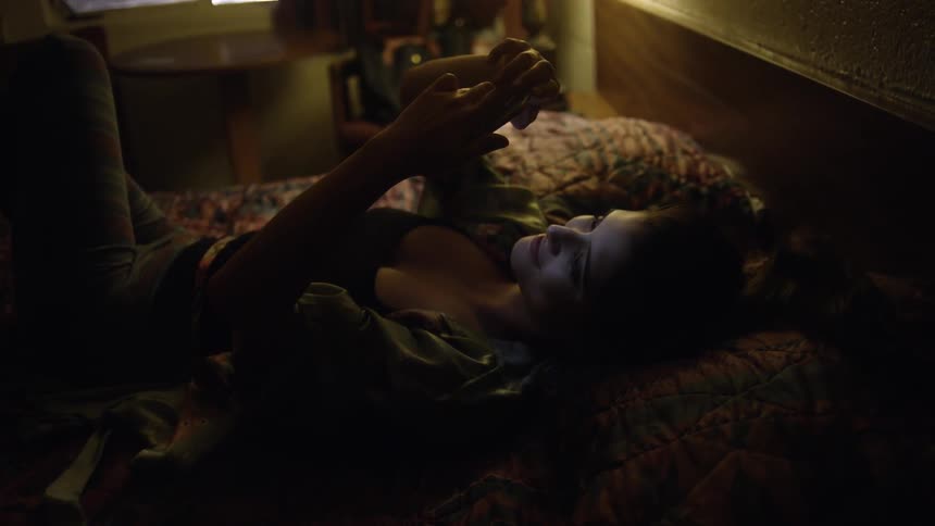 A woman lies on a bed looking at her phone