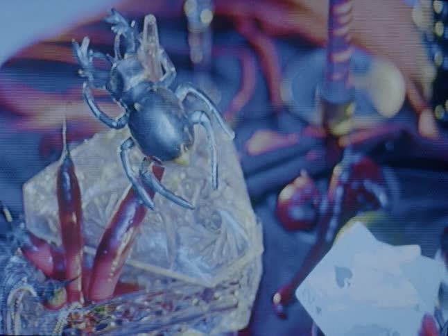 A closeup of a metallic scarab figurine on a decorative surface with red chilis under changing lights possibly part of an artistic or craft display