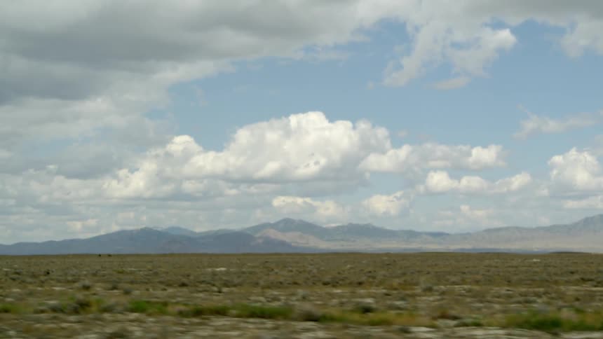 White clouds hang above a flat landscape near mountains