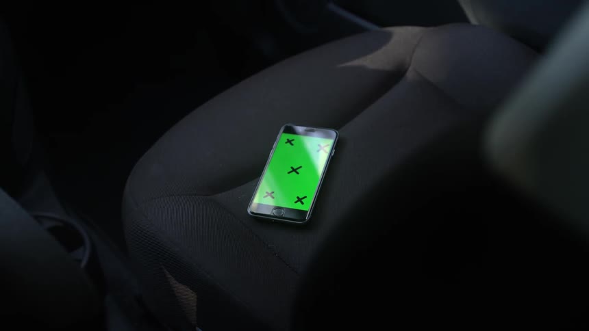 A phone with a green screen rests on a car seat