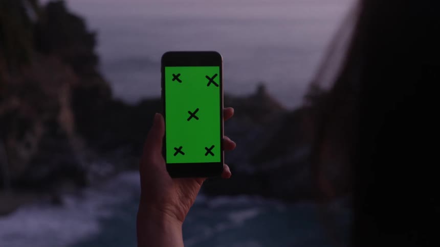 A person is holding up a phone by a cliff