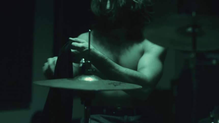 Male drummer sitting in front of a drum set puts on a shirt