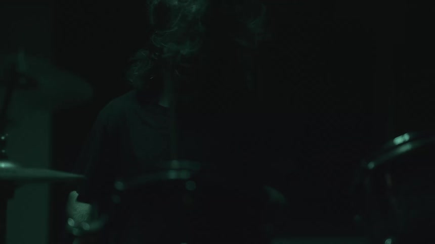 A man is playing the drums in a dark lit room