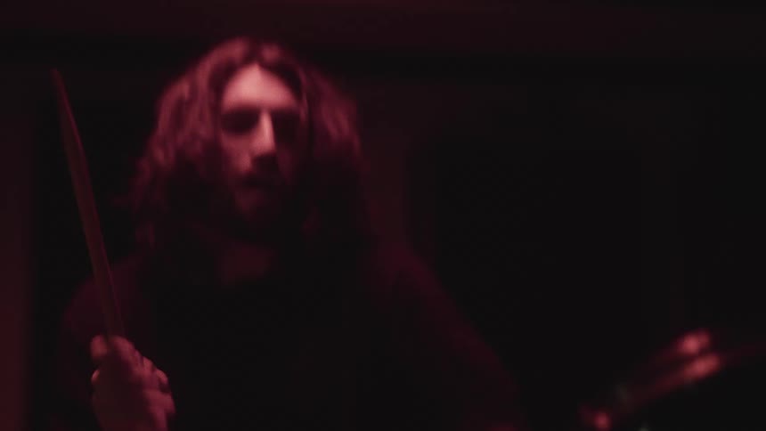 A man is playing the drums while sitting in a dark room