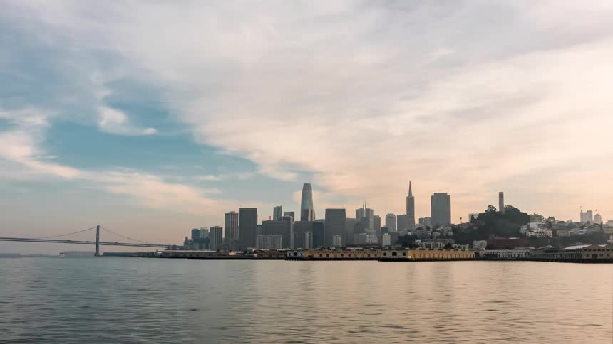 A distant cityscape silhouette of san francisco is visible across the bay under a partly cloudy sky with the bay bridge to the left