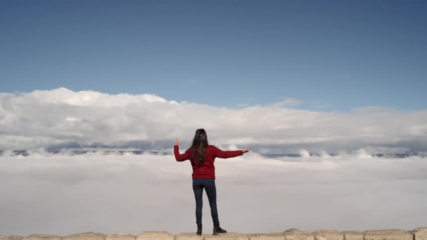 A woman dances on a ledge up in the clouds