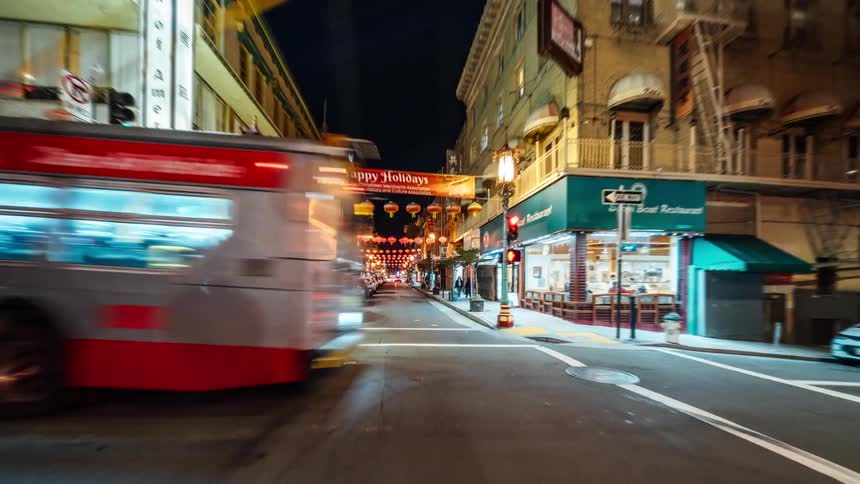 A pointofview timelapse traverses a chinatown street capturing the blur of moving cars and pedestrians amidst changing light conditions beneath hanging lanterns