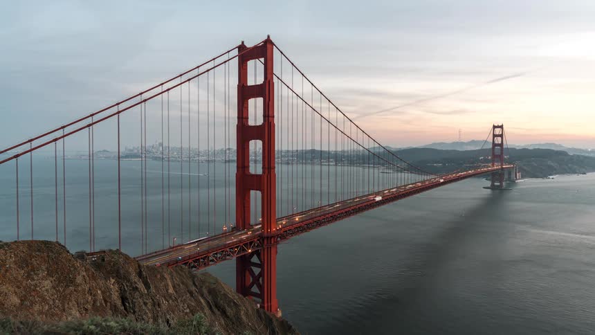 A timelapse captures the transition from day to night over the golden gate bridge showing changing skies and the structure illuminating as traffic flows