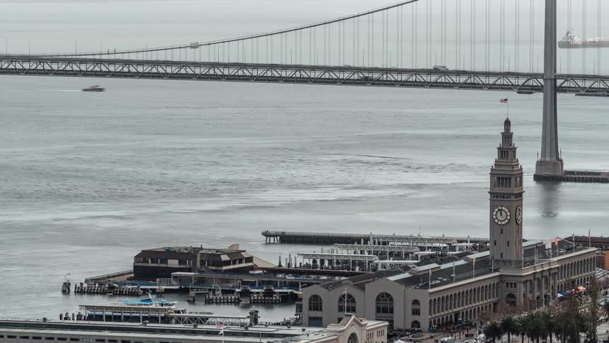 Ferries zip around the san francisco ferry building and traffic flows over the bay bridge in this elevated timelapse utilizing a tiltshift effect to create a miniature world