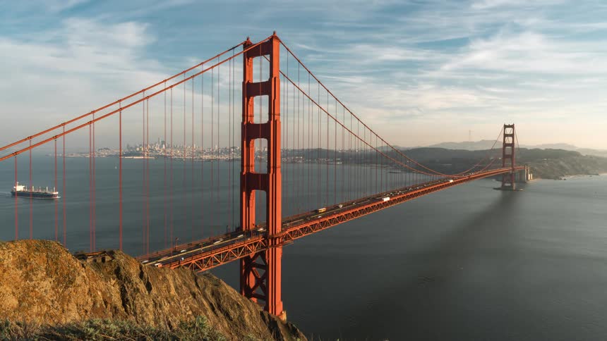 A timelapse captures the golden gate bridge with spedup car traffic crossing fastmoving clouds overhead and a tanker ship passing underneath