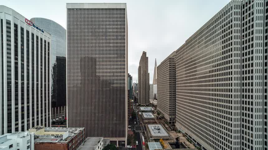 Towering city buildings frame a busy street below where cars and buses appear as miniatures speeding through this tiltshift timelapse shot