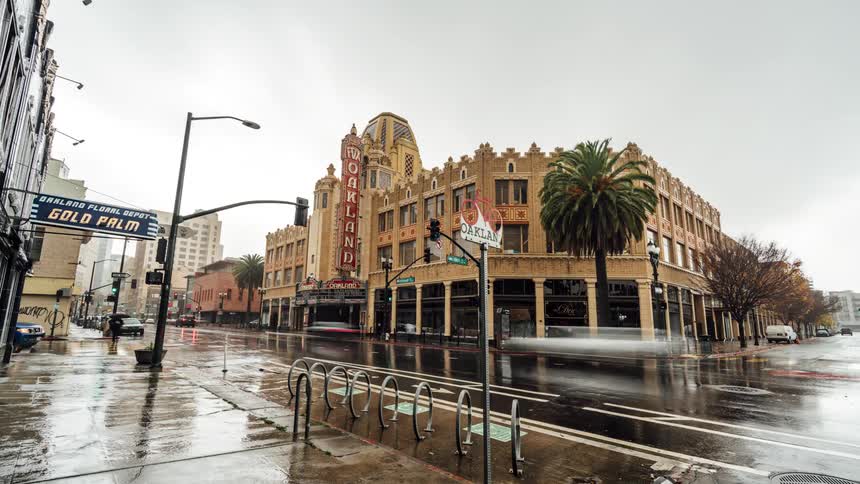 A large theatre sits on a rainy street corner below an overcast sky as vehicles fly by