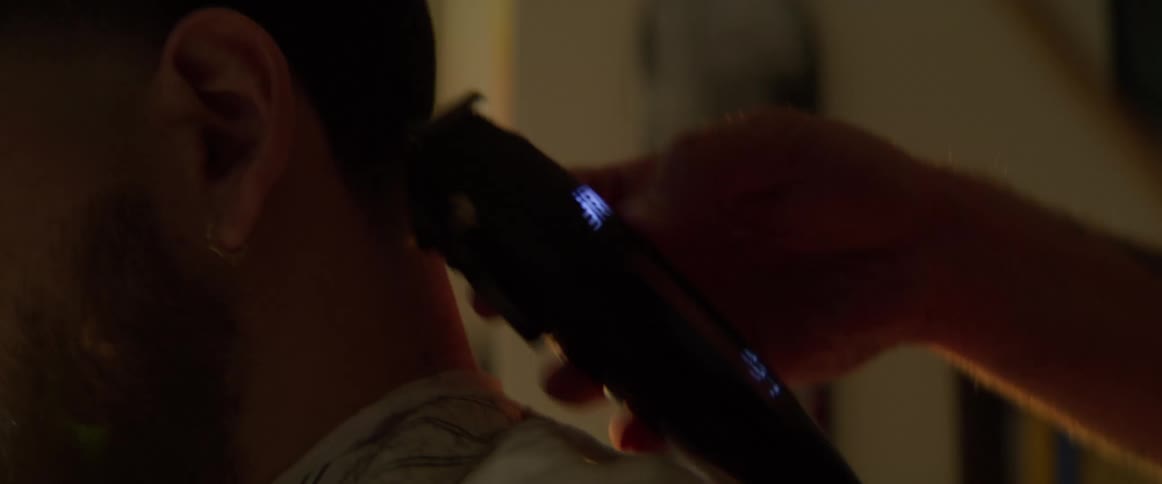 Male barber uses hair trimmers while giving a customer a hair cut