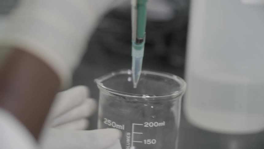 Scientist takes something from a beaker and puts into a tube