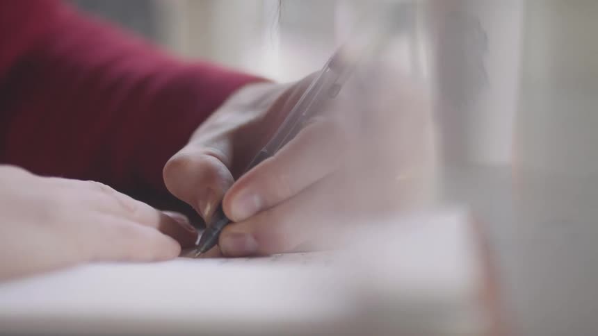 A woman is writing in the notebook with a pen