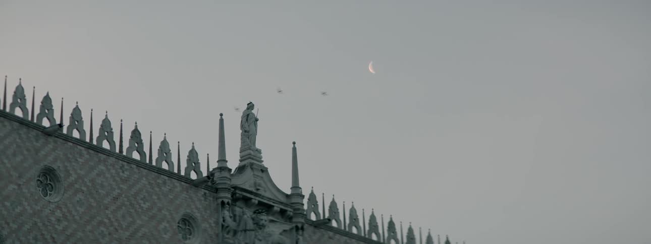 A partial moon is above this stone building