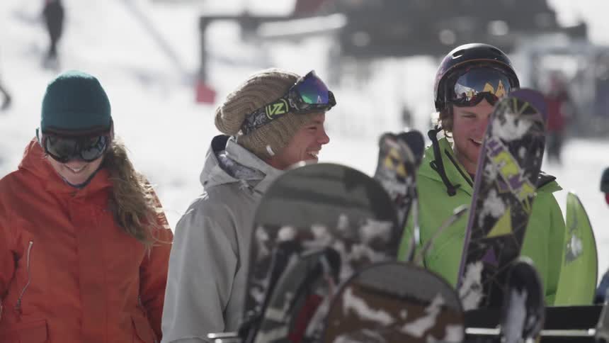 Group of skiers smile and walk toward the ski and snowboard rack