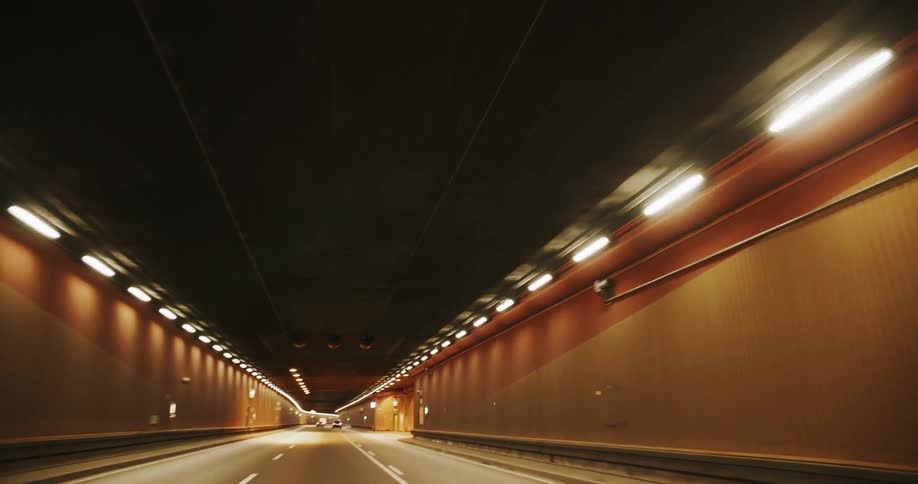 A long empty tunnel stretches into the distance illuminated by rows of warm evenly spaced lights along its walls