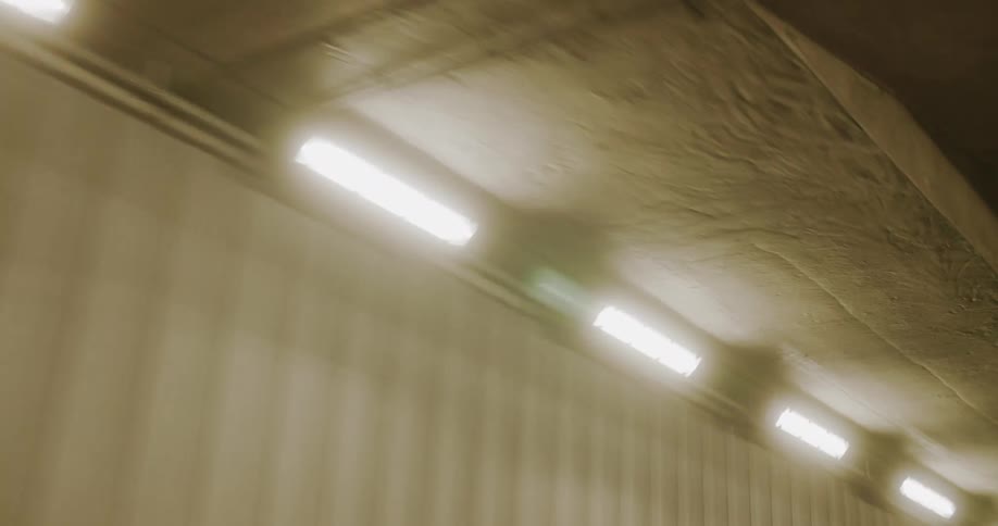 A tunnel is lit up by intermittent lights on both sides near the ceiling
