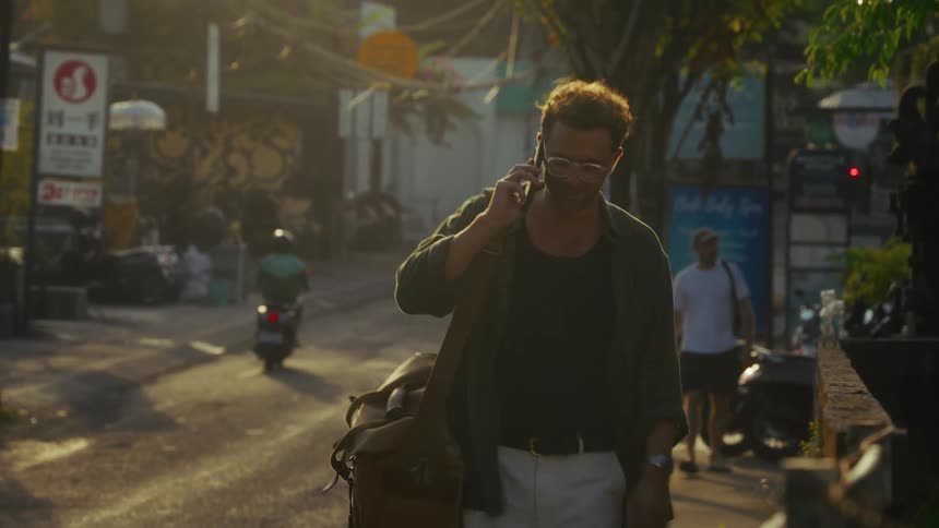 A man is walking down the block while talking on his phone