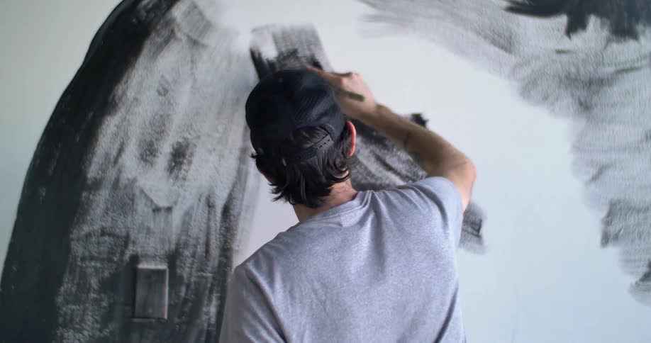 A man is painting on a canvas with black paint