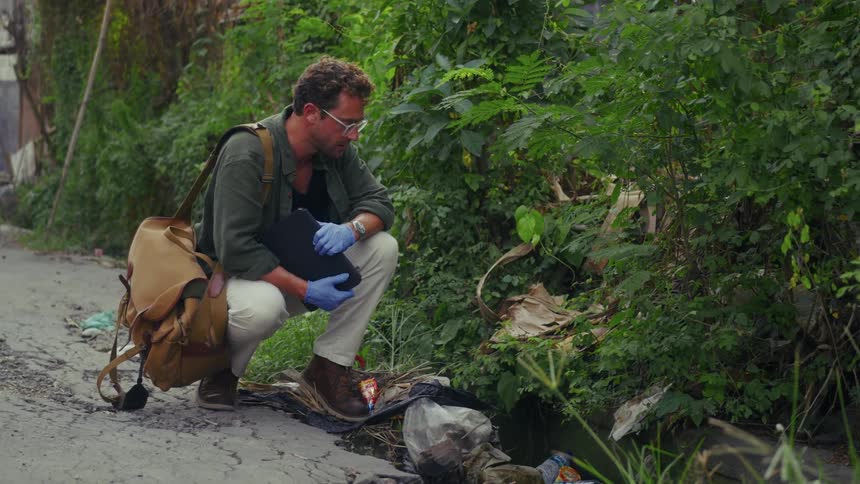 A man is holding his tablet near some trash