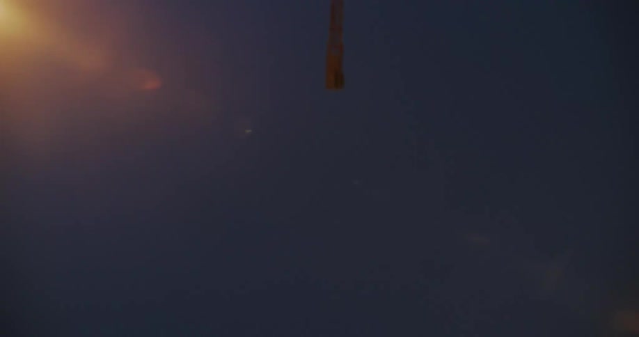 A lowangle shot shows the underside of an overpass with a glimpse of a distant cityscape against a twilight sky