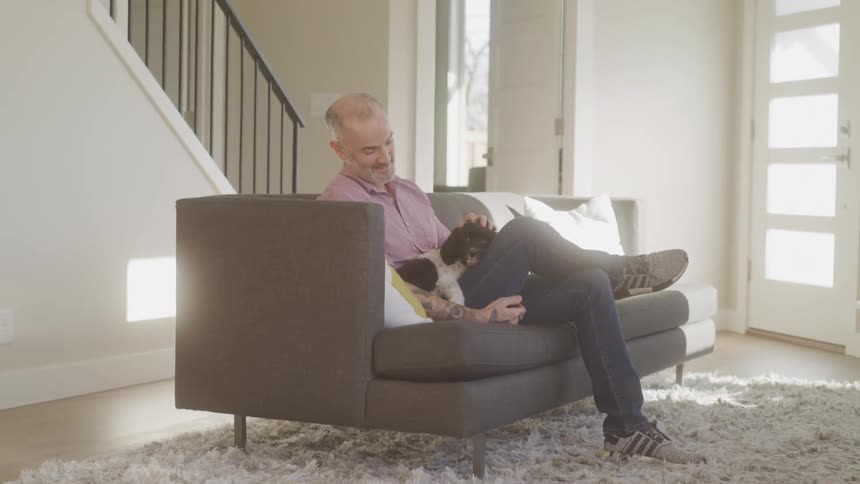 A man is petting his dog on the couch