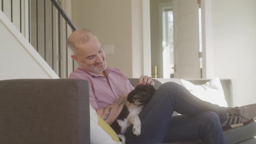 Dog dad happily sitting on couch petting his dog lovingly