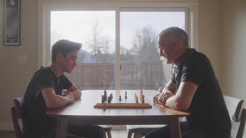 Father and son playing chess on dining room table