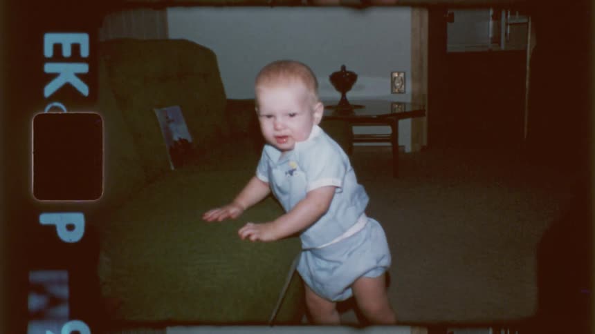 A baby smiles while walking by the couch