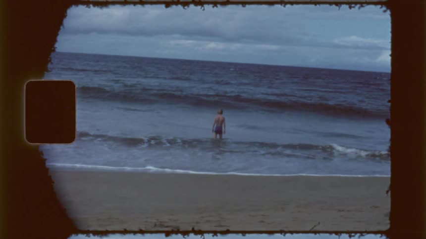 Young boy wades in the ocean on a cloudy day