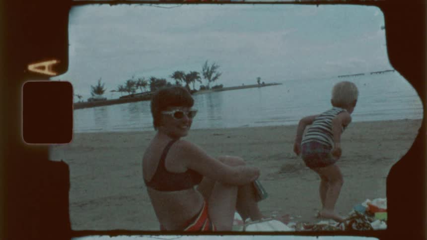 A mother smiles as her son runs on the beach